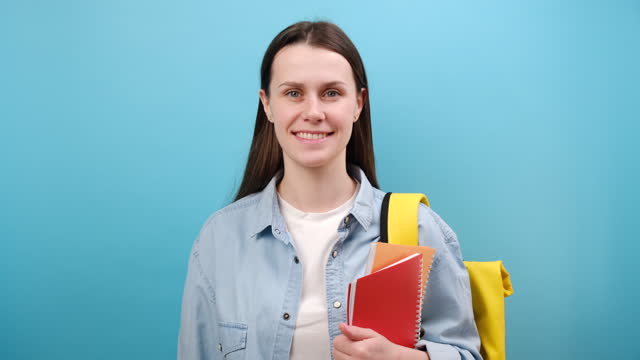 Portrait of secret blinking woman student in shirt with backpack say hush be quiet with finger on lips shhh gesture, isolated over blue background. Education in high school university college concept