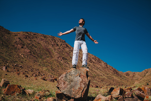 Handsome successful man standing with closed eyes on a huge boulder in mountains