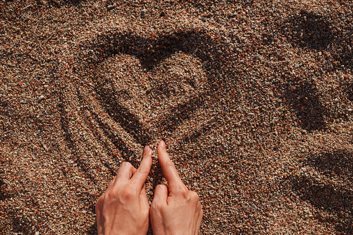 Woman hands drawing heart shape in the sand at summer day