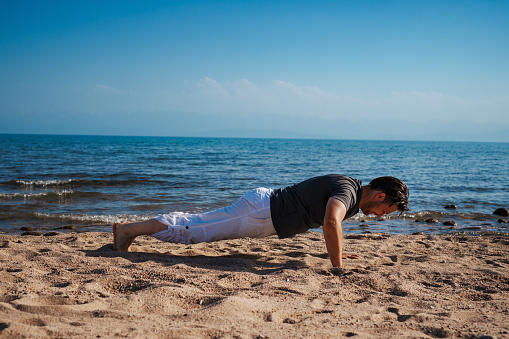 Sports young man doing push-ups on the beach