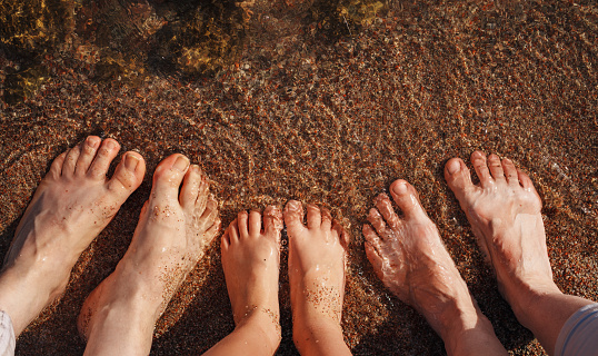Parents and child feet on sea beach in water at summer day