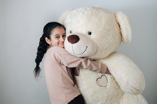 Studio shot of 13 years old cheerful girl with lots of emotions raising her teddy and having fun. Tenderness