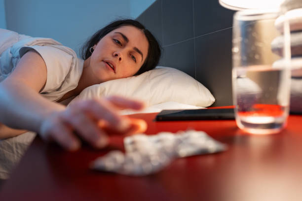 caucasian adult woman reaches for red bedside table with medicines. defocused hand and sleeping pills in close-up. concept of insomnia, sleep disorders and headache - narcotic medicine pill insomnia imagens e fotografias de stock