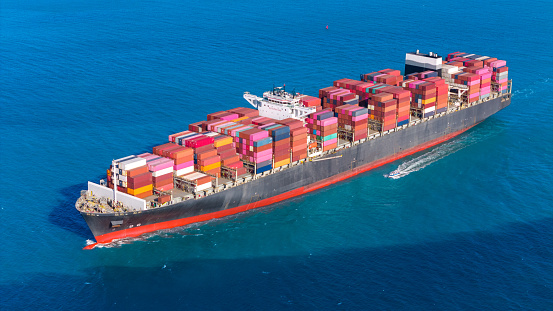 Front view of a loaded container cargo vessel traveling with speed over blue ocean