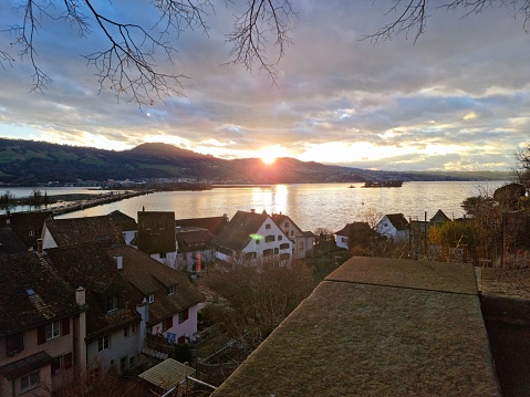 The image shows the historic city of Rapperswil with the lake of Zurich at sunset during winter season