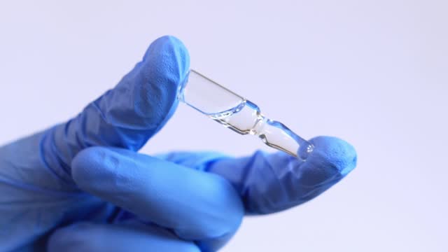 Woman's hand in a blue medical glove holds a glass ampoule