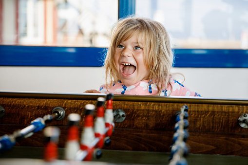Little preschool girl playing table soccer. Happy excited positive child having fun with family game with siblings or friends