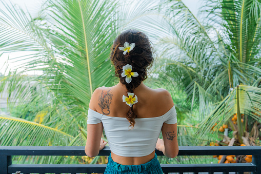Woman with frangipani flowers in her  braided hair on the background of lush greenery on tropical resort