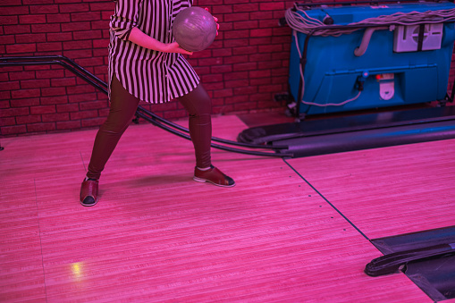 View of a girl throwing a ball down the bowling lane to knock down pins.