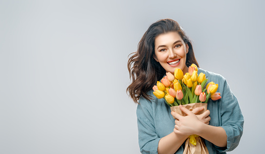 Beautiful young woman with yellow flowers in hands on grey wall background.