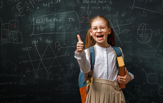 Back to school. Happy cute industrious child indoors. Kid is learning in class on background of blackboard.