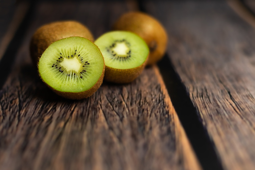 Whole and cut kiwi on a wooden brown table. Green fruits. Vitamin C. Fruits in the kitchen.