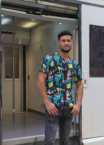handsome moroccan man standing and looking at camera outside a train waggon | hands in pockets