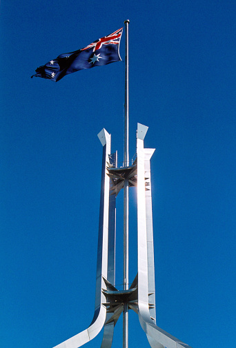 Canberra, ACT, Australia: New Parliament House - stainless steel pyramidal structure and flag mast with the Australian flag flying above Capital Hill, seen against blue sky.