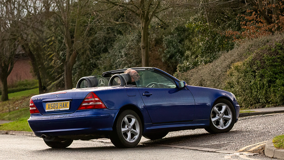 Milton Keynes,UK-Feb 4th 2024: 2000 blue Mercedes Benz SLK open top classic car  driving on an English road.