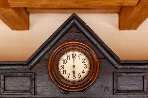 An antique German clock with a yellowed face is built into a roof-shaped brown wood cabinet.