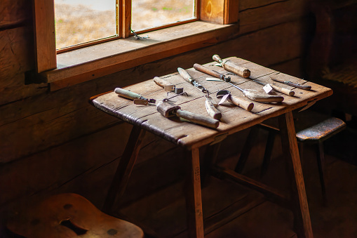 A set of antique woodcarving tools on a wooden table by the window. The craft of making clogs.