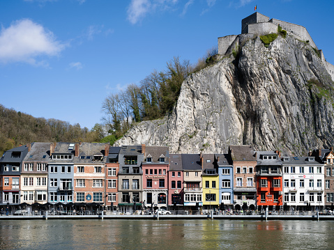 Colorful Dinant Cityscape at the waterfront of River Meuse under blue summer sky.  Huge limestone cliff with old Citadel of Dinant on the cliff top behind the town of Dinant. 102 MPixel Hasselblad X2D Cityscape. Dinant, Wallonia, Namur, Belgium, Europe.