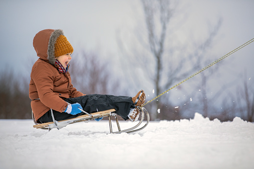 A very joyful emotion of a child when riding a sled on fluffy snow on a beautiful winter day. Portrait in profile, winter nature background.