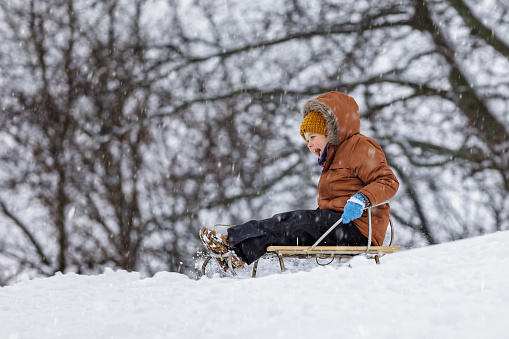 Cheerful boy on sled outdoors in winter snow.