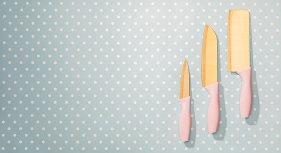 Three various-sized kitchen knives with pink handles are neatly aligned against a pastel blue polka dot backdrop.