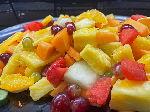 A large bowl of fruit salad at a delicatessen counter display.   Chopped fruit including pineapple, watermelon, grapes, and cantaloupe.