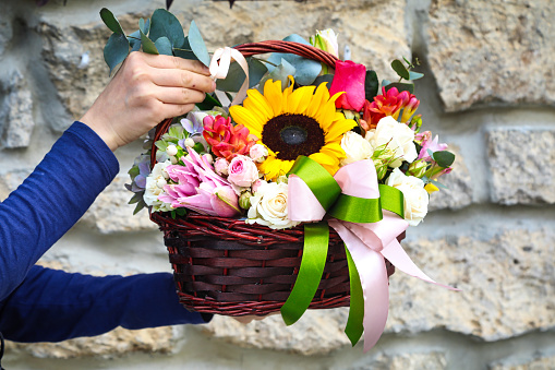 A person is holding a basket filled with beautiful flowers, providing ample white copy space.
