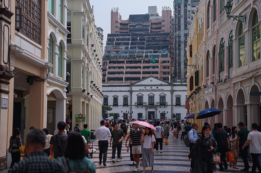 Macao, China - May 12, 2023: A diverse group of individuals walking down a lively urban street lined with tall buildings.