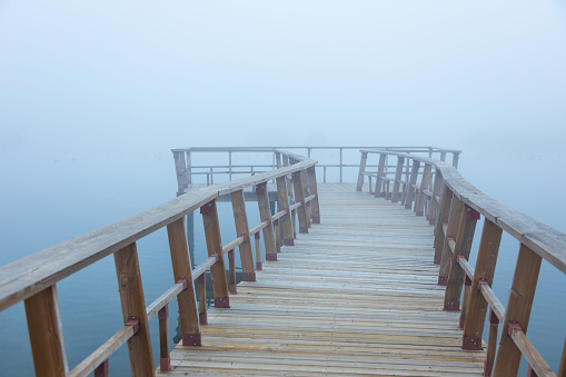 A straight wooden pier disappearing into the dense fog over a serene lake