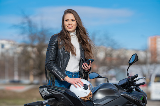 Female motorcyclist going on a road trip, traveling on a motorbike and using smartphone