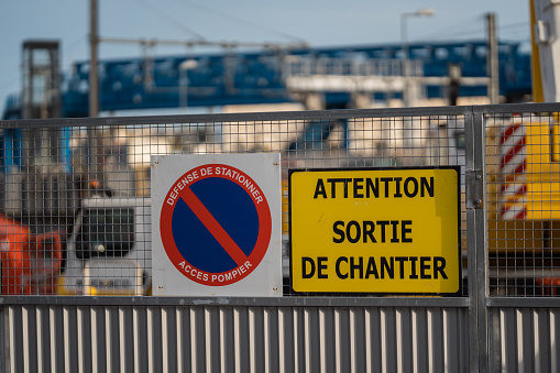 Various warning signs posted on the fence of a construction site. Attention Exit from the construction site in french.