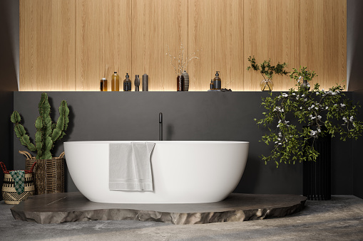 Modern white bathtub standing on marble podium in modern bathroom with black and wooden wall. Bathroom background.