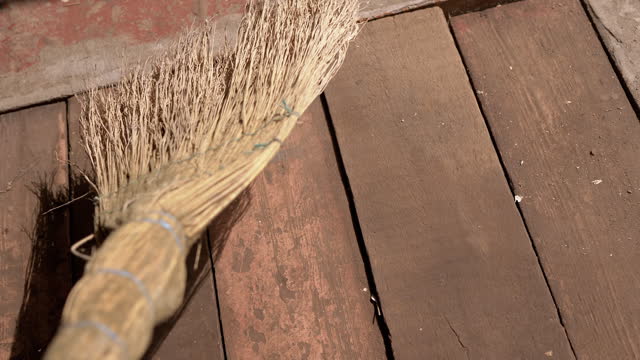 Person Sweeping an Old Dirty Wooden Floor with Broom in the Garage in Sunlight