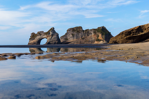 Rock formations reflect in the water. Archway Islands view at Wharariki Beach, New Zealand