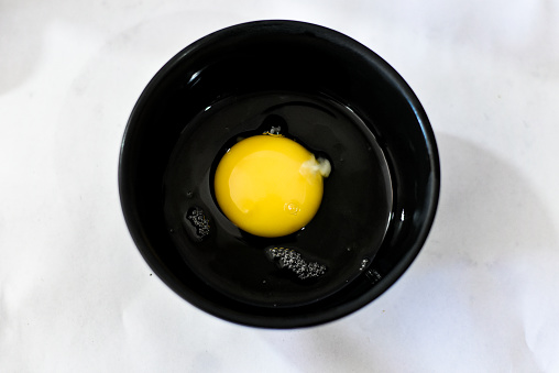 A black bowl full of egg yolk and egg white.