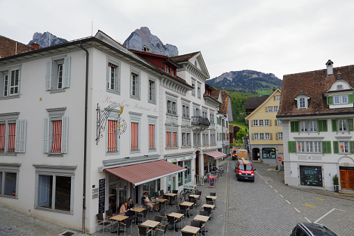 Schwyz, Switzerland - May 09, 2016: Buildings in the town square, and there are several people in the outdoor restaurant that can be seen in the distance. There is also some traffic.