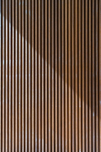 Crop of luxury room wall decorated with panels made of natural wood. Vertical timber slats texture used in minimalistic interior design for simple and elegant effect. High quality photo