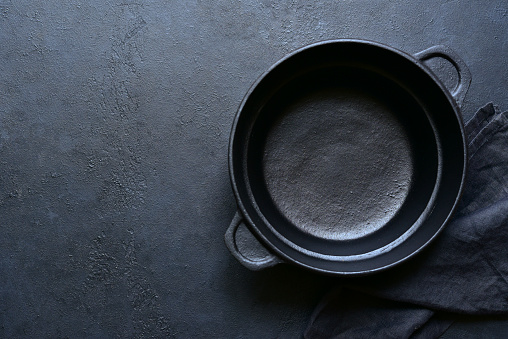 Culinary background with empty cast iron pan , napkin and spoon on a black slate, stone or concrete background. Top view with copy space.