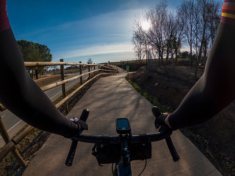 Riding on a gravel bicycle on a cycling way with a fence next to an asphalt road rider point of view