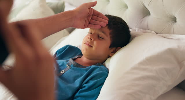 Phone call, parent and sick child with a fever in bed at a house, nursing flu or virus. Boy kid, illness and bedroom with a person, concern and hand on forehead while talking to family doctor contact
