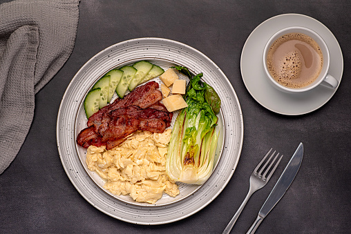Food photography of breakfast; scrambled egg; fried bacon, cucumber, bok choi; cheese parmesan, keto diet; brunch;  background;