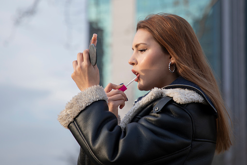 A young beautiful woman refreshing her lipstick in city life