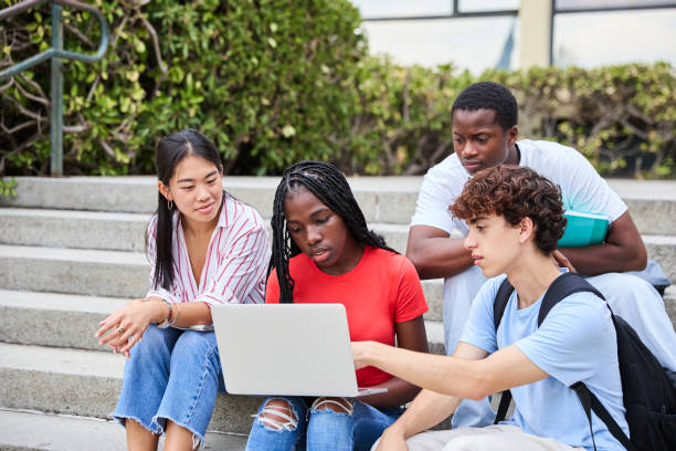 Young multiethnic students in casual clothes with backpacks sitting on stone stairs and studying on laptops. Concept of education and friendship.