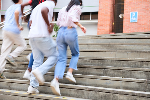 Group of unrecognisable young students running up the school stairs