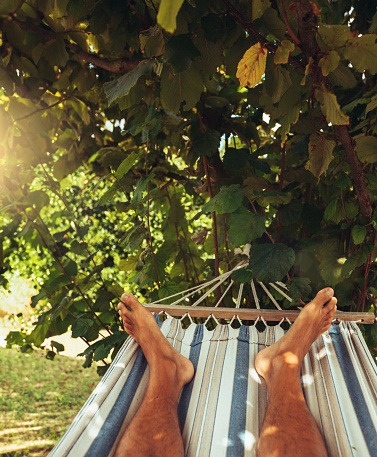 POV of summer relaxing and sunbathing on hammock: man feet while resting under a warm sun in Italy