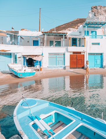 Wooden door closed and three glass windows with open shutters blue color on white wall background. Cyclades island house front view, Greek traditional architecture.