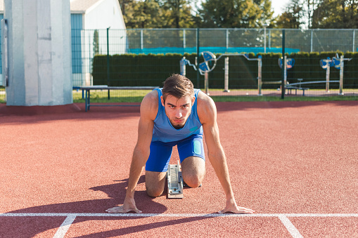 Runner using starting block to start his run on race track. Runner using starting block to start his run on running track in a stadium. Athlete starting his sprint on an all-weather running track.