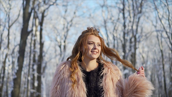 Beautiful Russian girl in fur mink coat and colorful scarf on winter landscape. Stylish girl in a fur coat in the winter park.