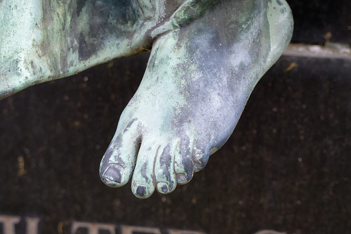 weathered bare foot of a cemetery angel statue on a grave with blurred gravestone in the background