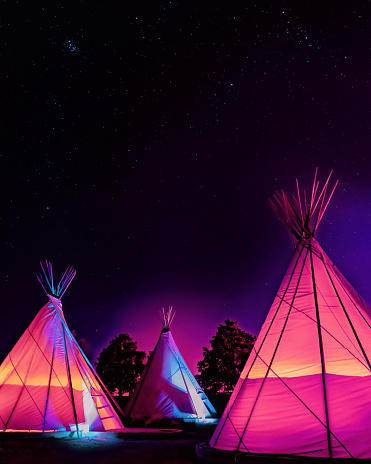 Three vaporwave-style teepees glowing at night under stars in Marfa, Texas